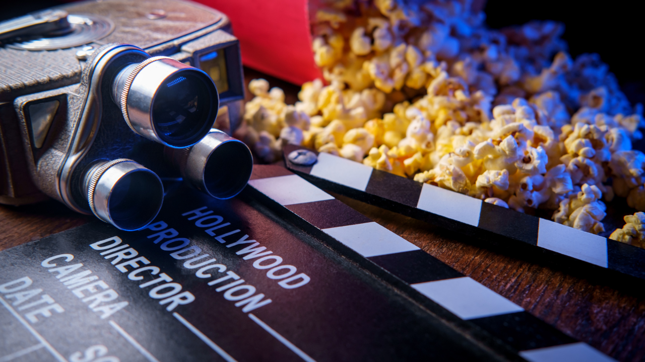 A camera is sitting on top of a clapper board next to a bucket of popcorn.