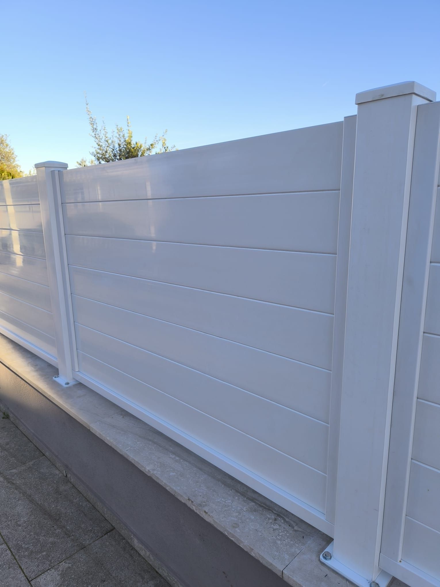 Recinzione bianca con listelli orizzontali e pali quadrati, all'esterno in una giornata di sole.