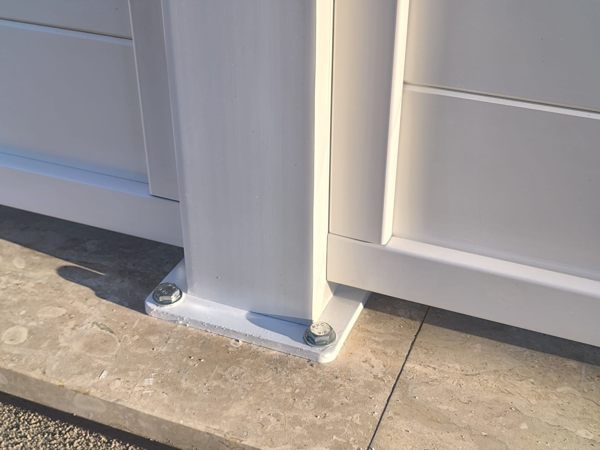 Palo del cancello in metallo bianco imbullonato a una superficie di cemento.