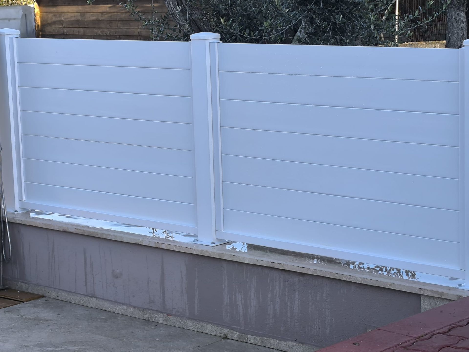 Recinzione bianca con listelli orizzontali su un muretto basso in cemento.