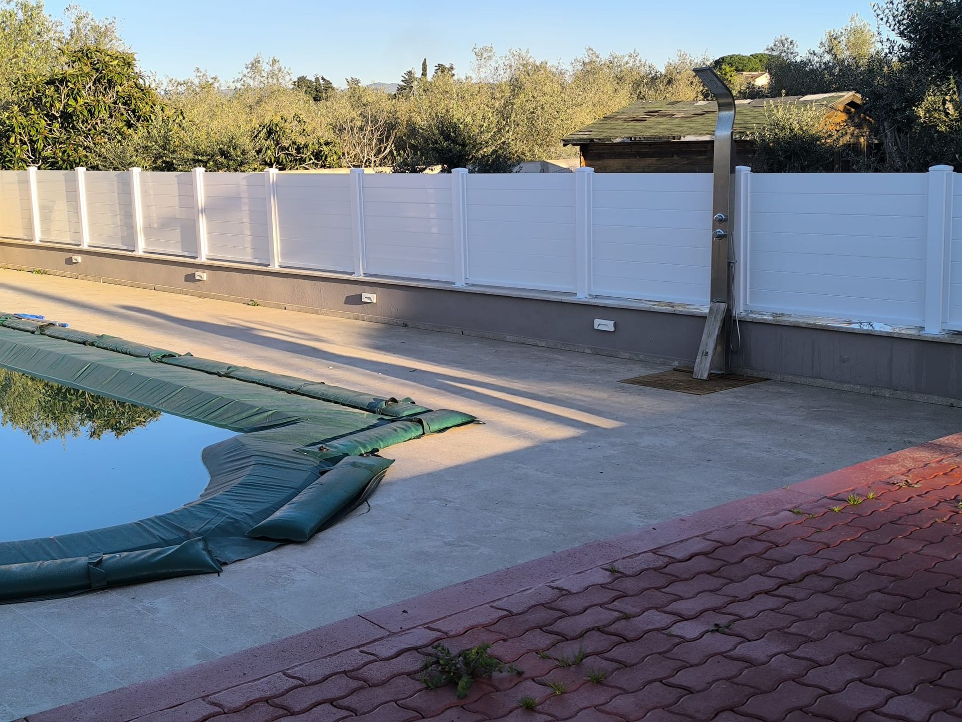 Recinzione bianca che circonda la piscina. Copertura verde sull'acqua. Patio pavimentato.