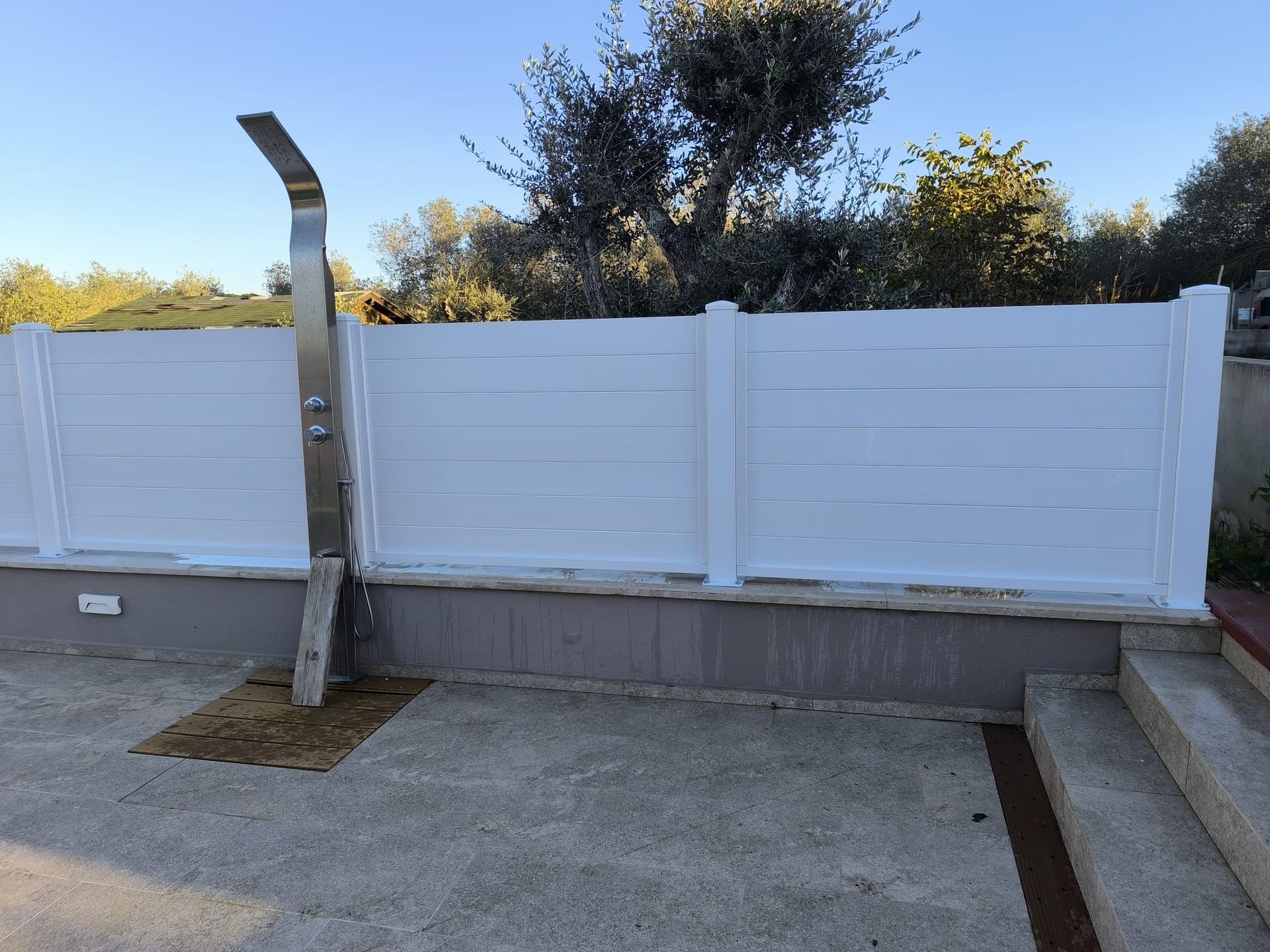 Recinzione orizzontale bianca con doccia esterna accanto.