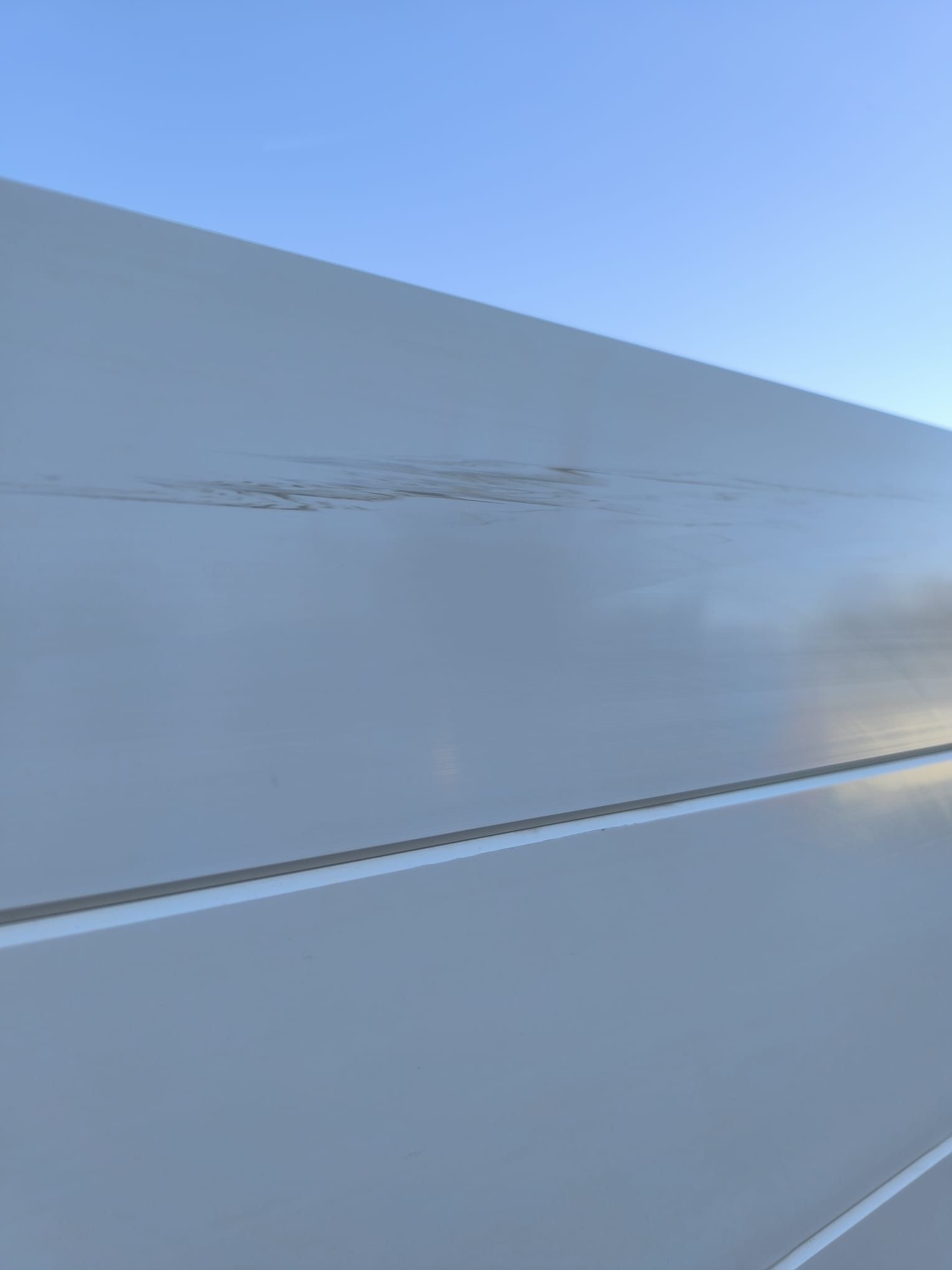 Esterno bianco di un edificio industriale danneggiato, contro un cielo blu.