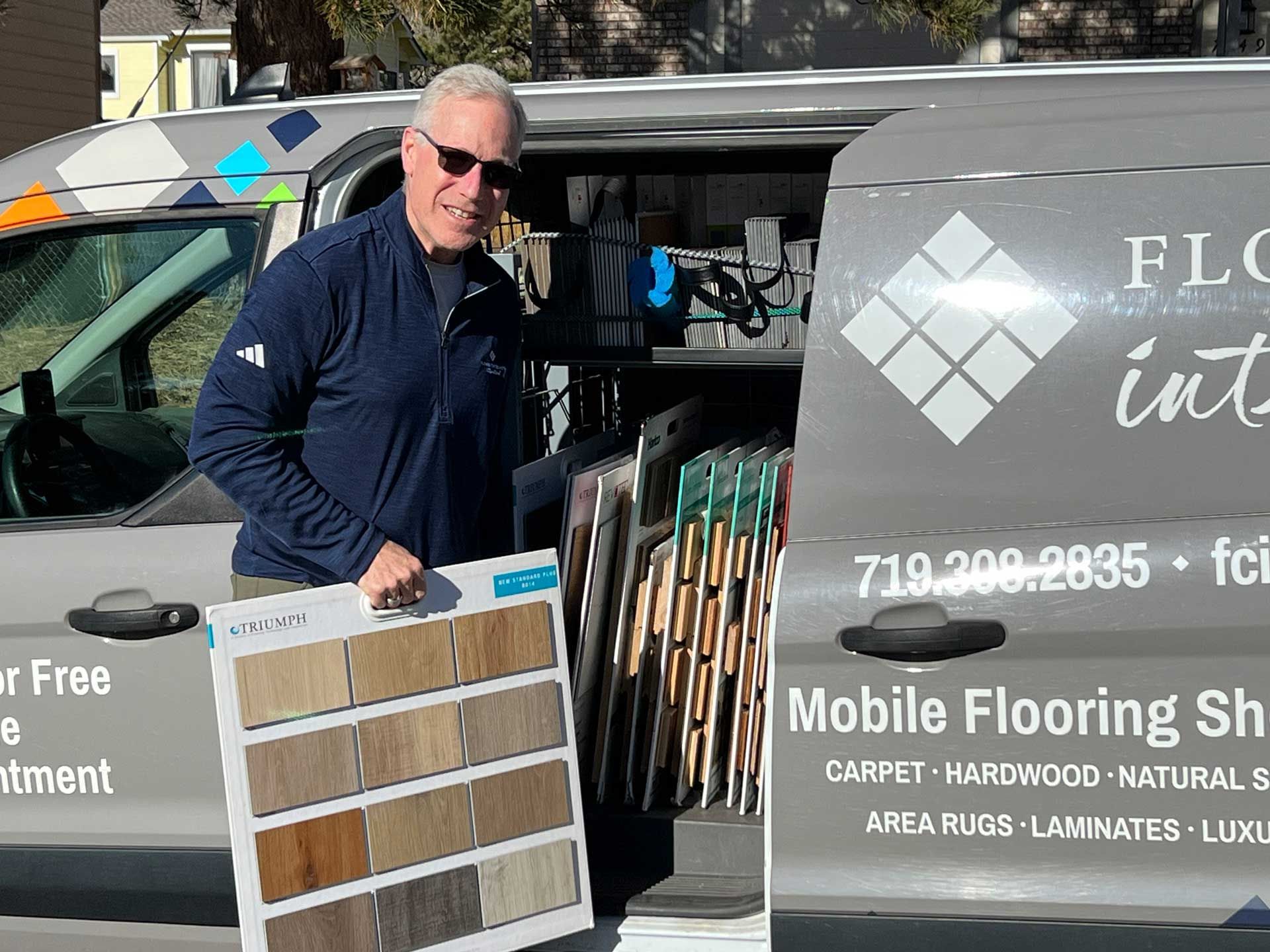 A man is standing in front of a van that says mobile flooring showroom.
