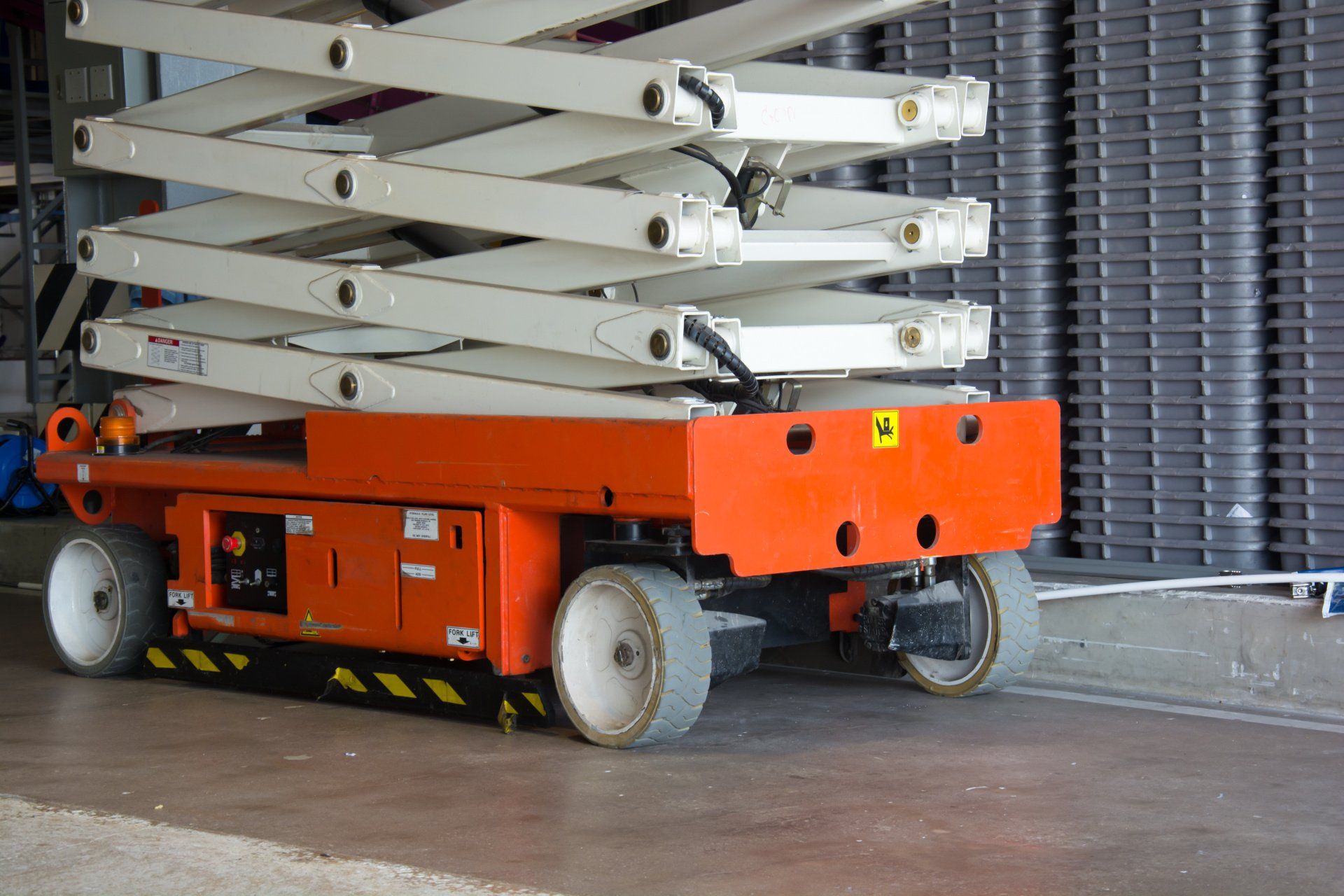 An orange and white scissor lift is parked in a warehouse.