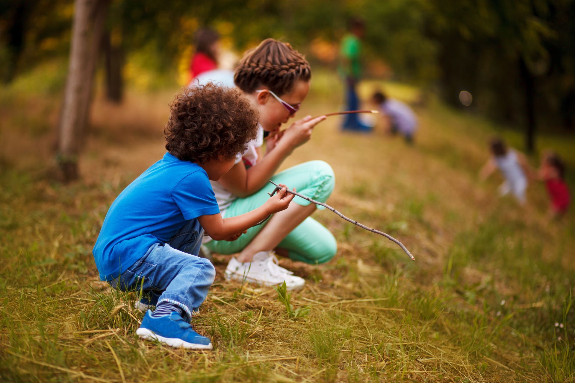 A boy and a girl are sitting in the grass looking through a stick
