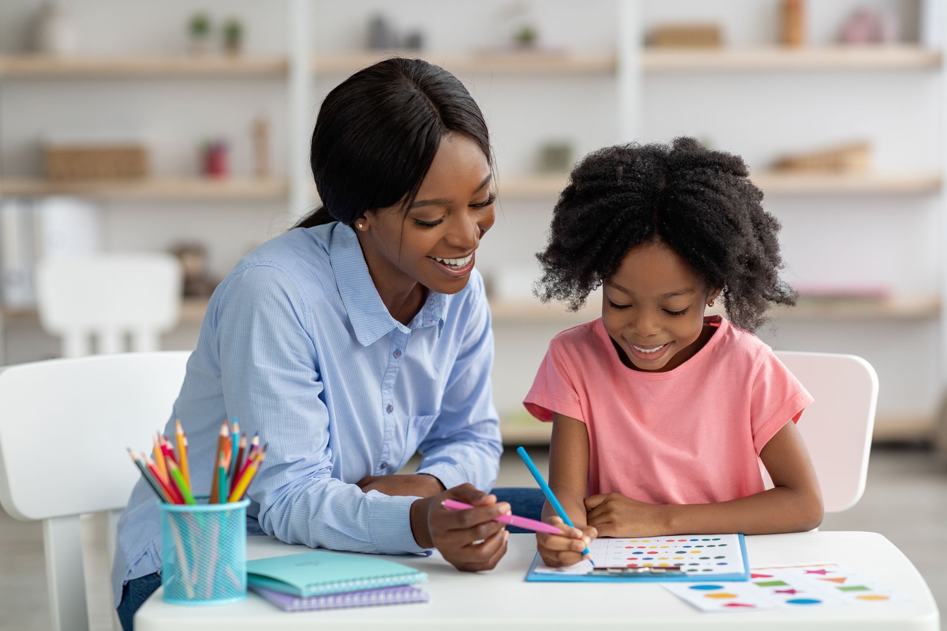 A woman is helping a little girl with her homework at a table