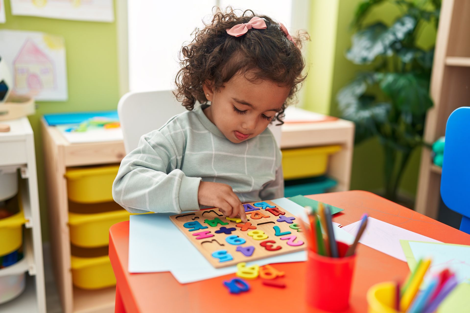 A little girl is sitting at a table playing with a wooden puzzle