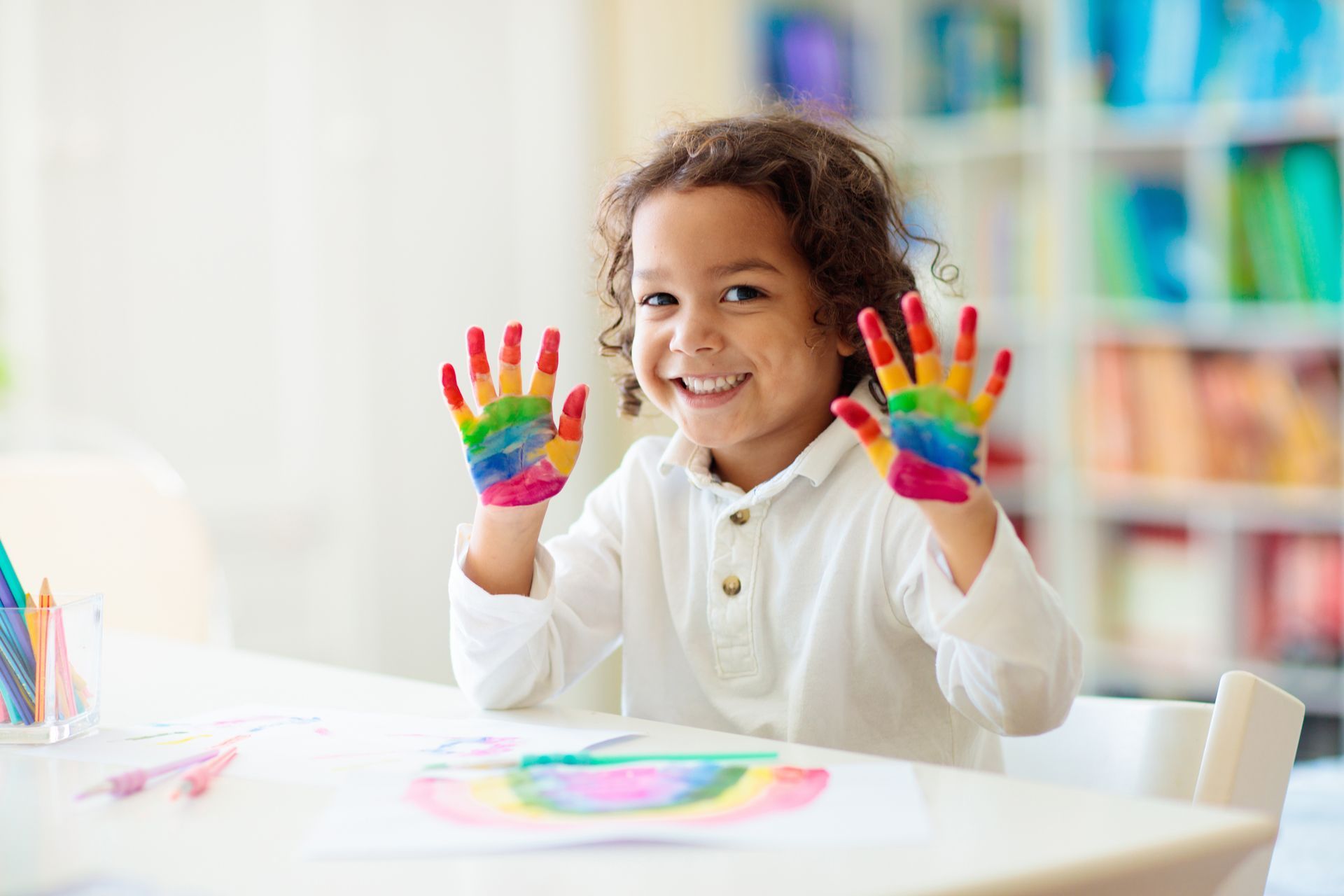 A little boy is sitting at a table with his hands painted in different colors