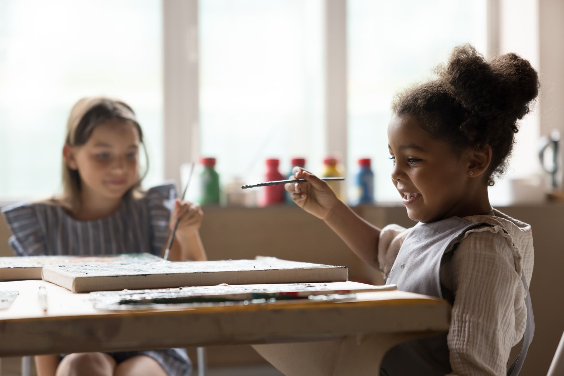 Two young girls are sitting at a table painting with watercolors