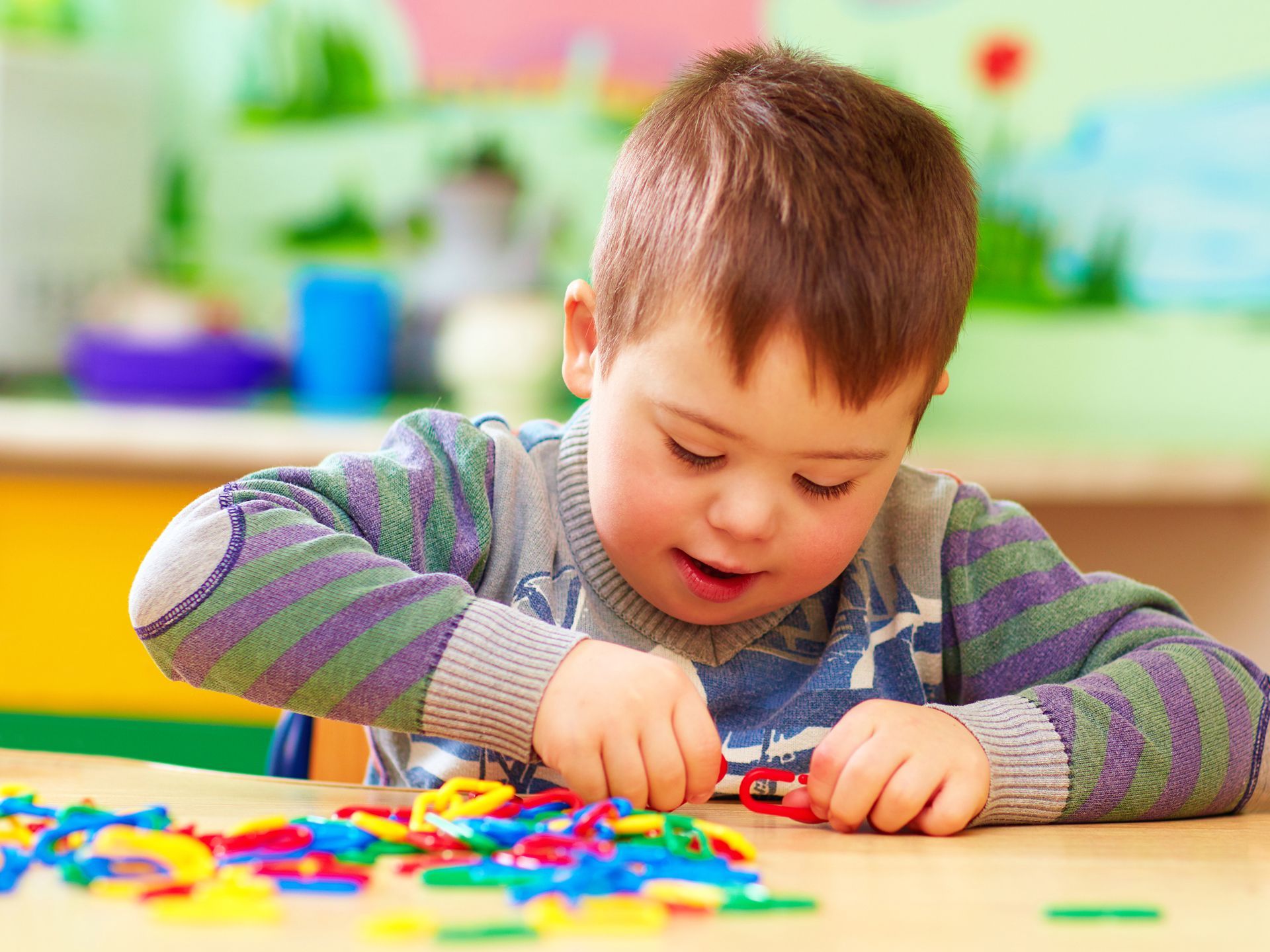A young boy with down syndrome is sitting at a table playing with colorful toys