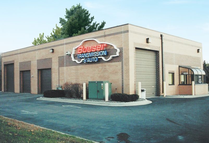 Exterior of a beige auto repair shop with a red-and-black sign and green door at a street corner | Boeser Automotive
