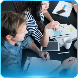 Two people at a table reviewing documents, using a tablet, and taking notes, in an office setting.
