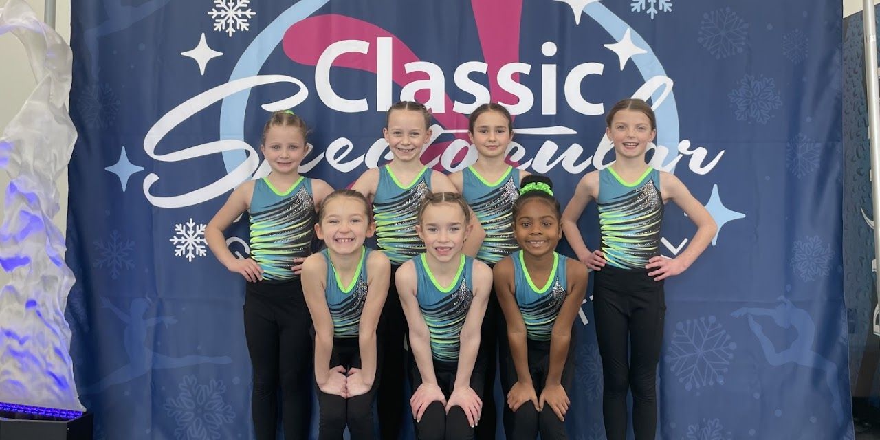 Group of young gymnasts in matching outfits posing in front of a banner.