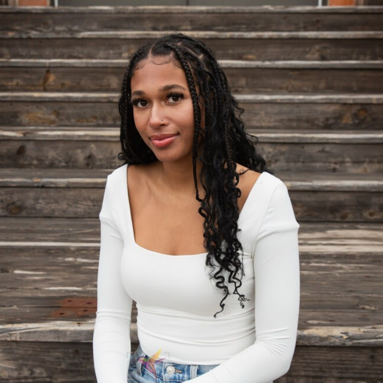 Woman with long braids, wearing white top, sitting on wooden steps.