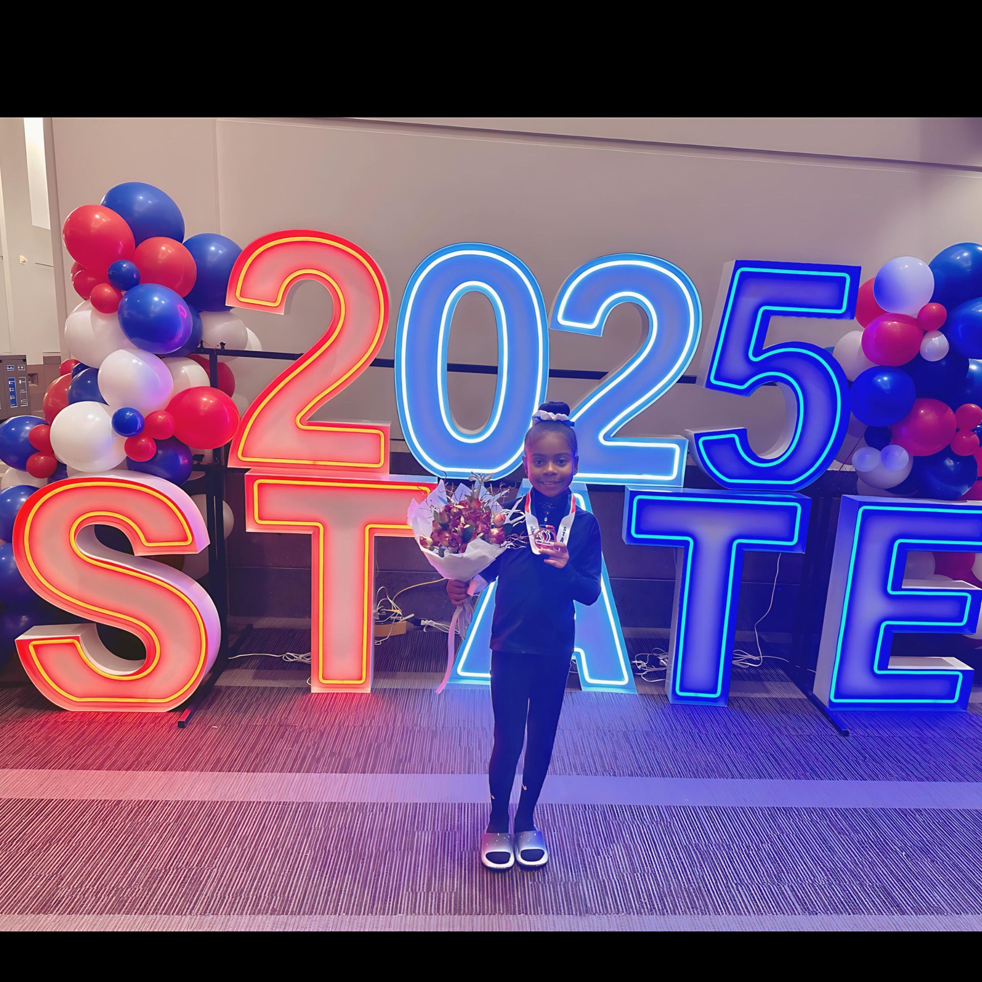 Girl smiling, holding flowers and a medal, in front of