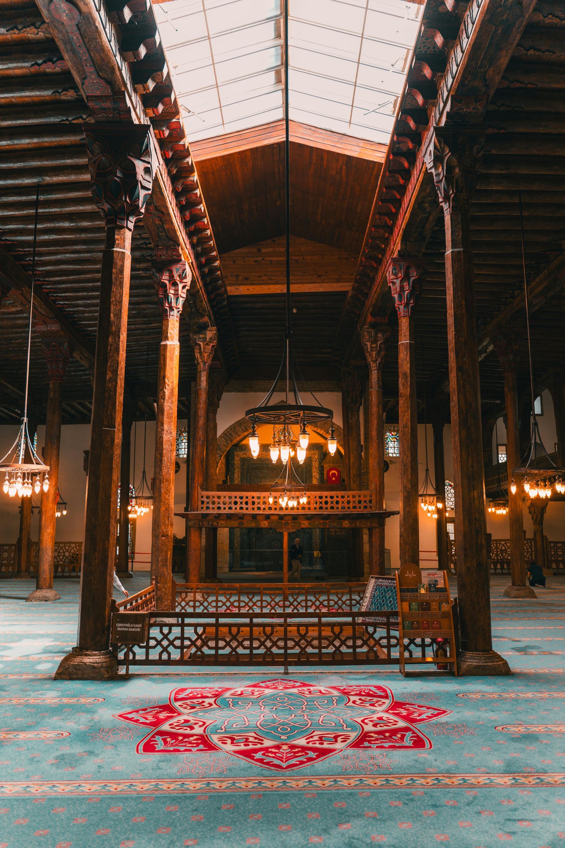 The inside of a mosque with wooden pillars and a rug on the floor.