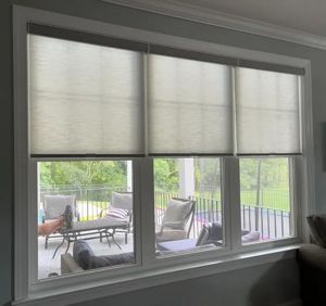 Three window shades partially covering a window that looks out onto a patio with furniture.