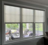 service Three window shades partially covering a window that looks out onto a patio with furniture.