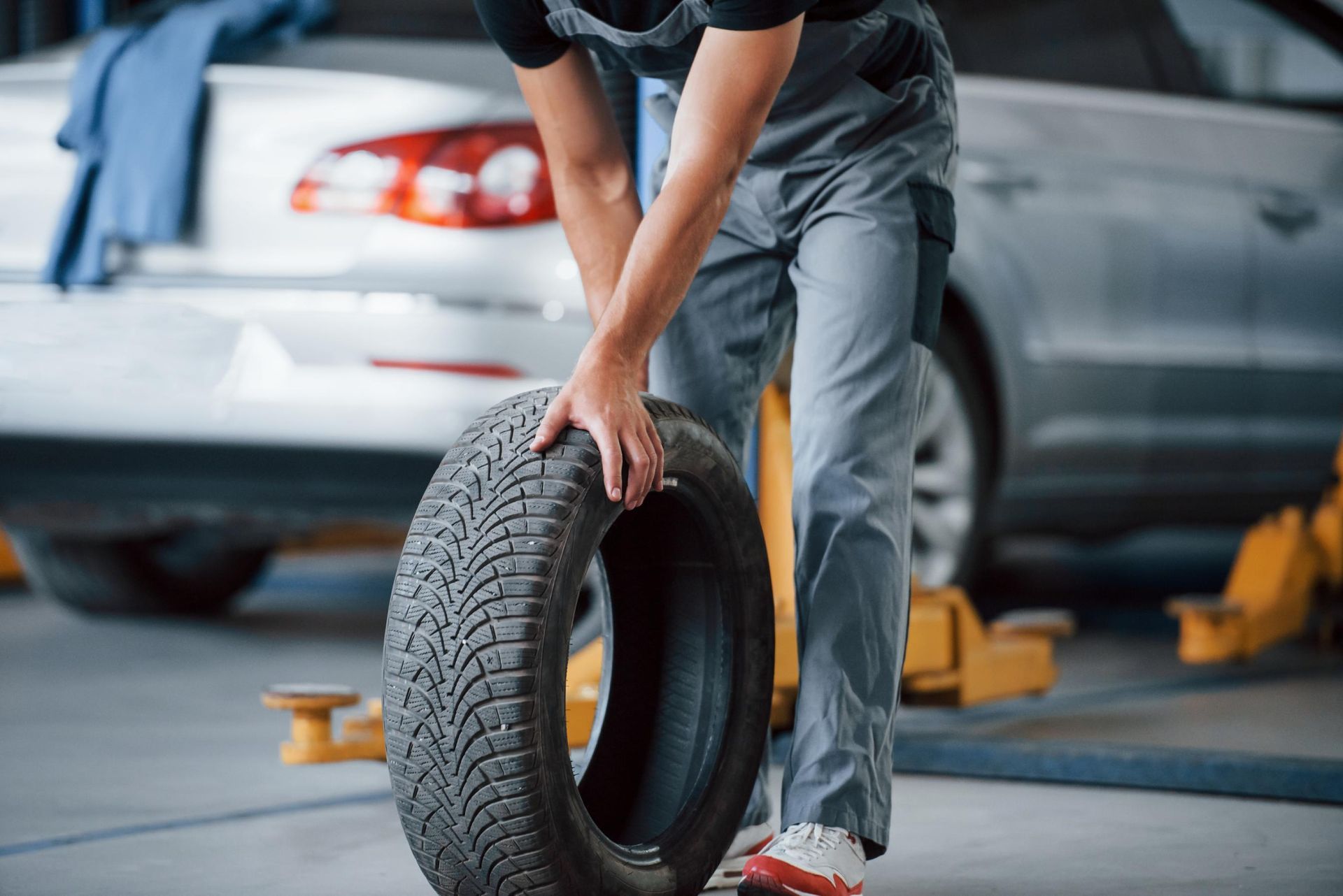 Person changing a tire beside a silver car in a garage, holding a black tire