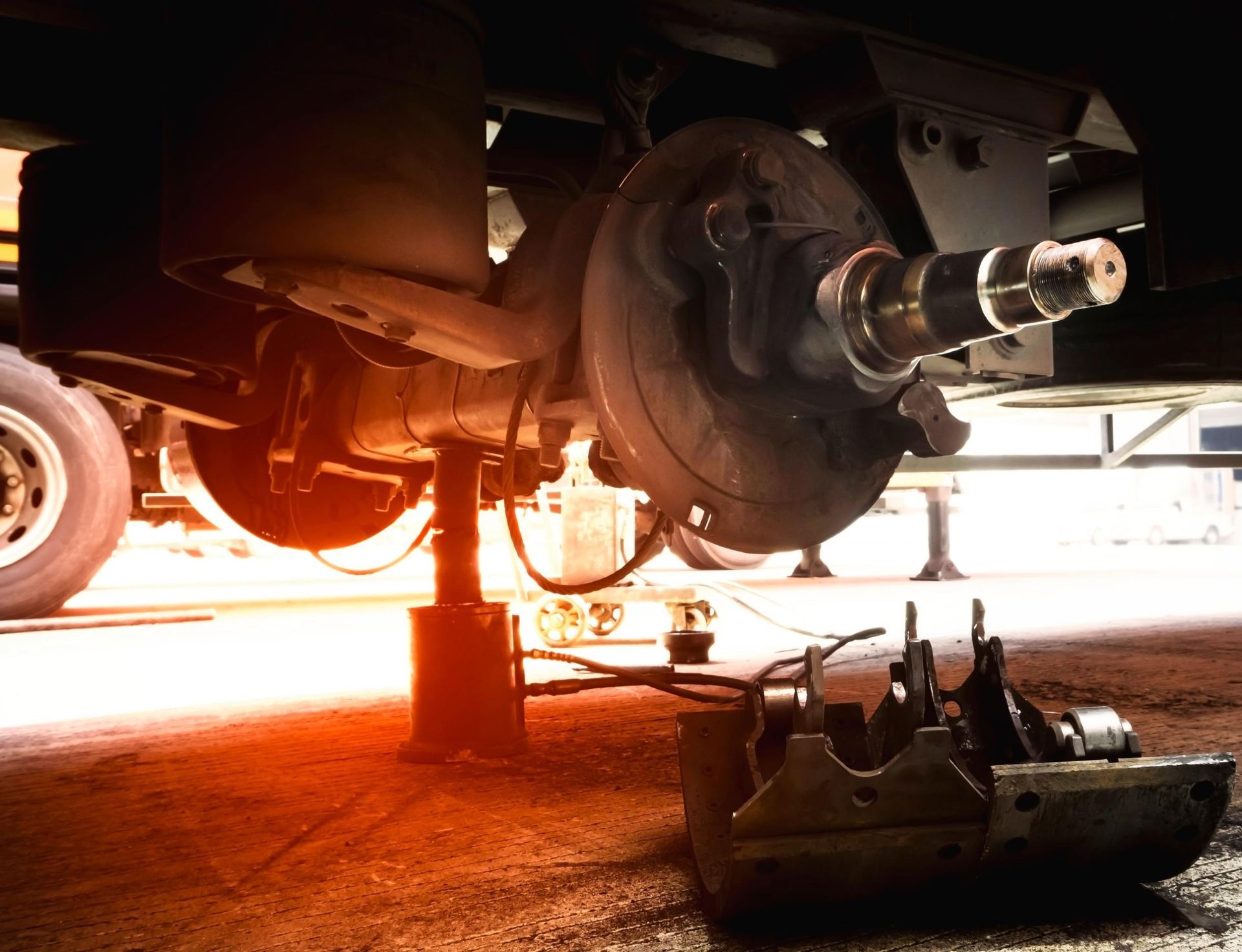 Car on jack with wheel removed, showing brake assembly and tools on the garage floor.