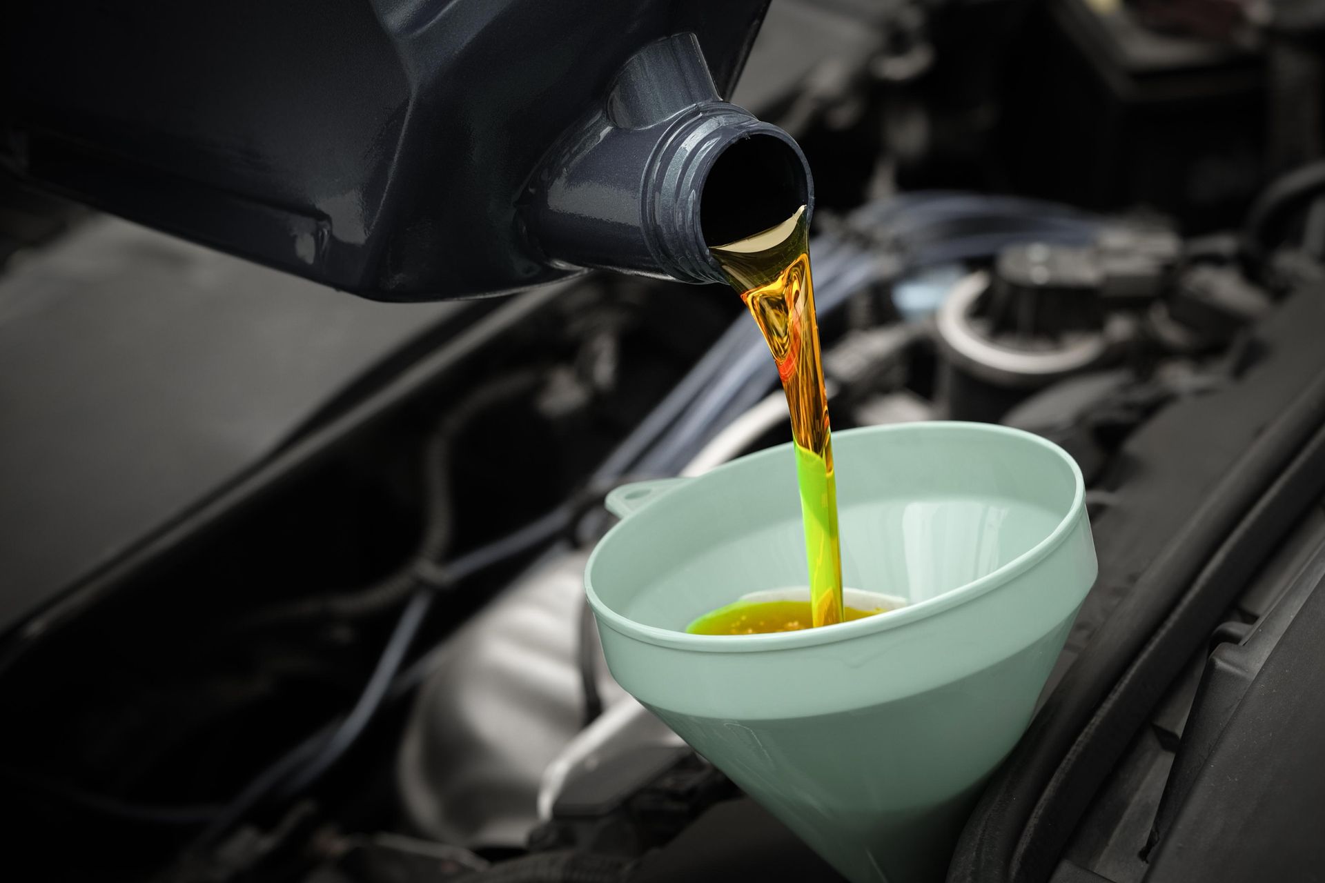 Oil being poured from a car engine into a green funnel in the engine bay.
