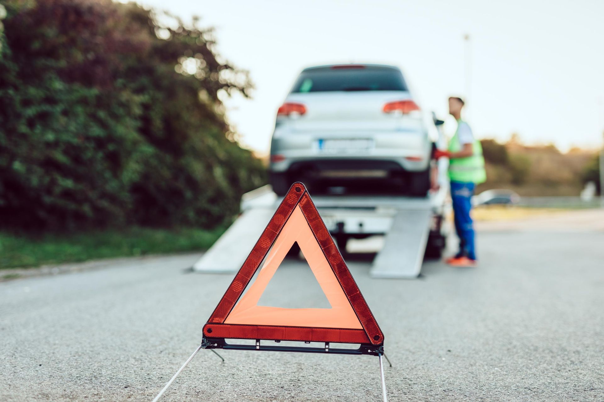 Warning triangle on road with car on tow truck and worker in background