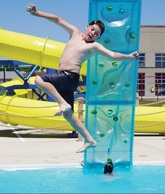 A shirtless boy is jumping into a pool near a water slide