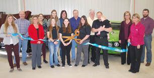 A group of people are standing in front of a green car holding scissors.