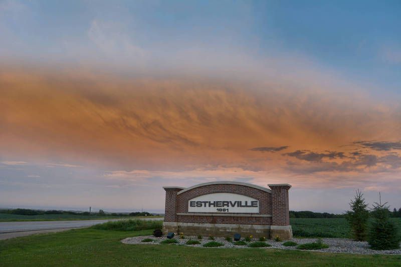 A brick sign in the middle of a grassy field with a sunset in the background.