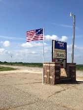 Two american flags are flying in front of a sign.