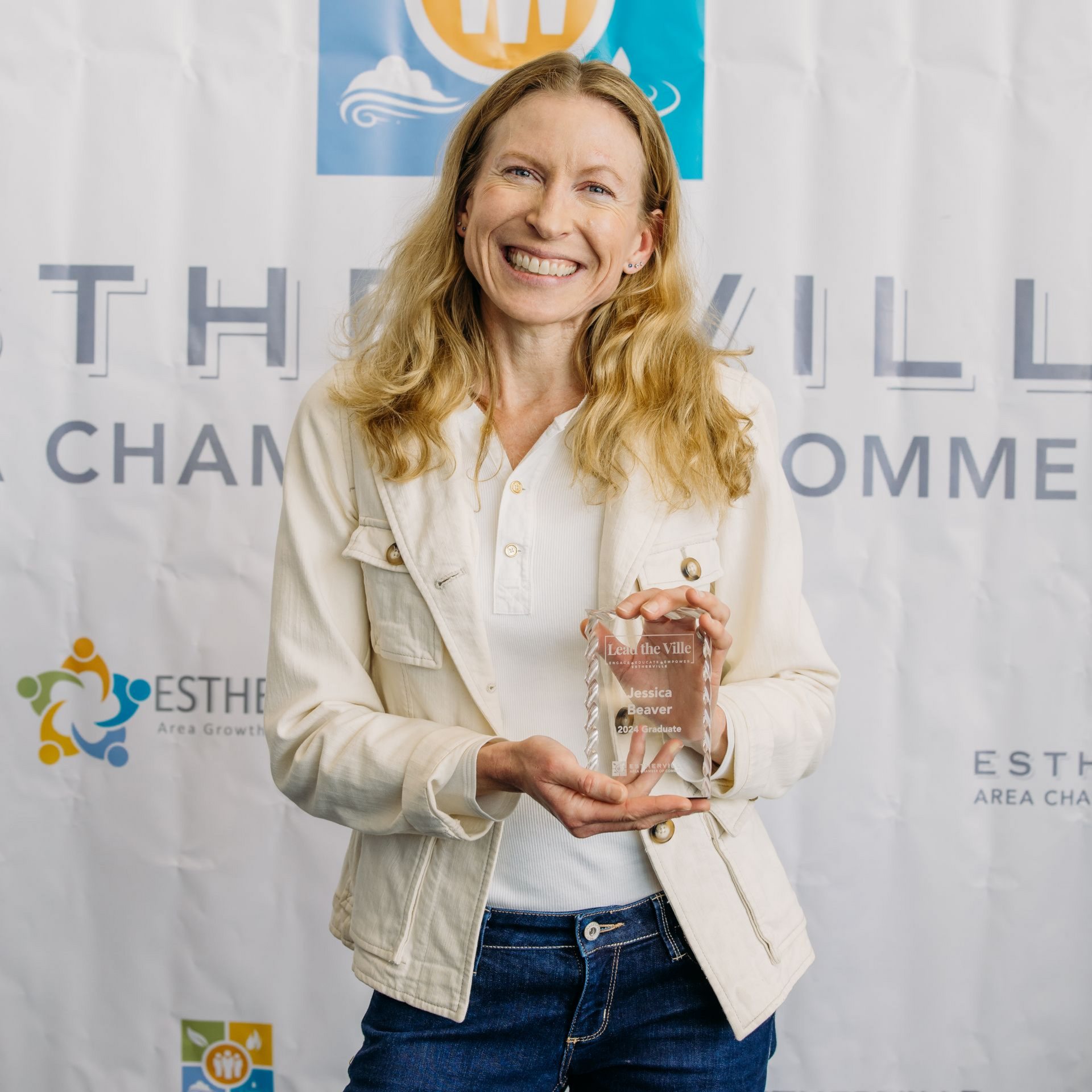 A woman is holding a trophy in front of a wall.