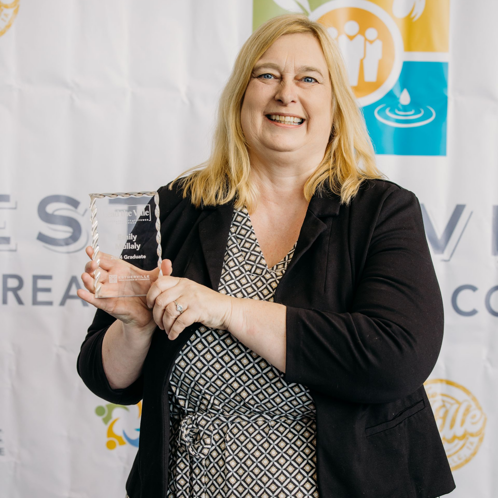 A woman is holding a trophy in front of a white backdrop.