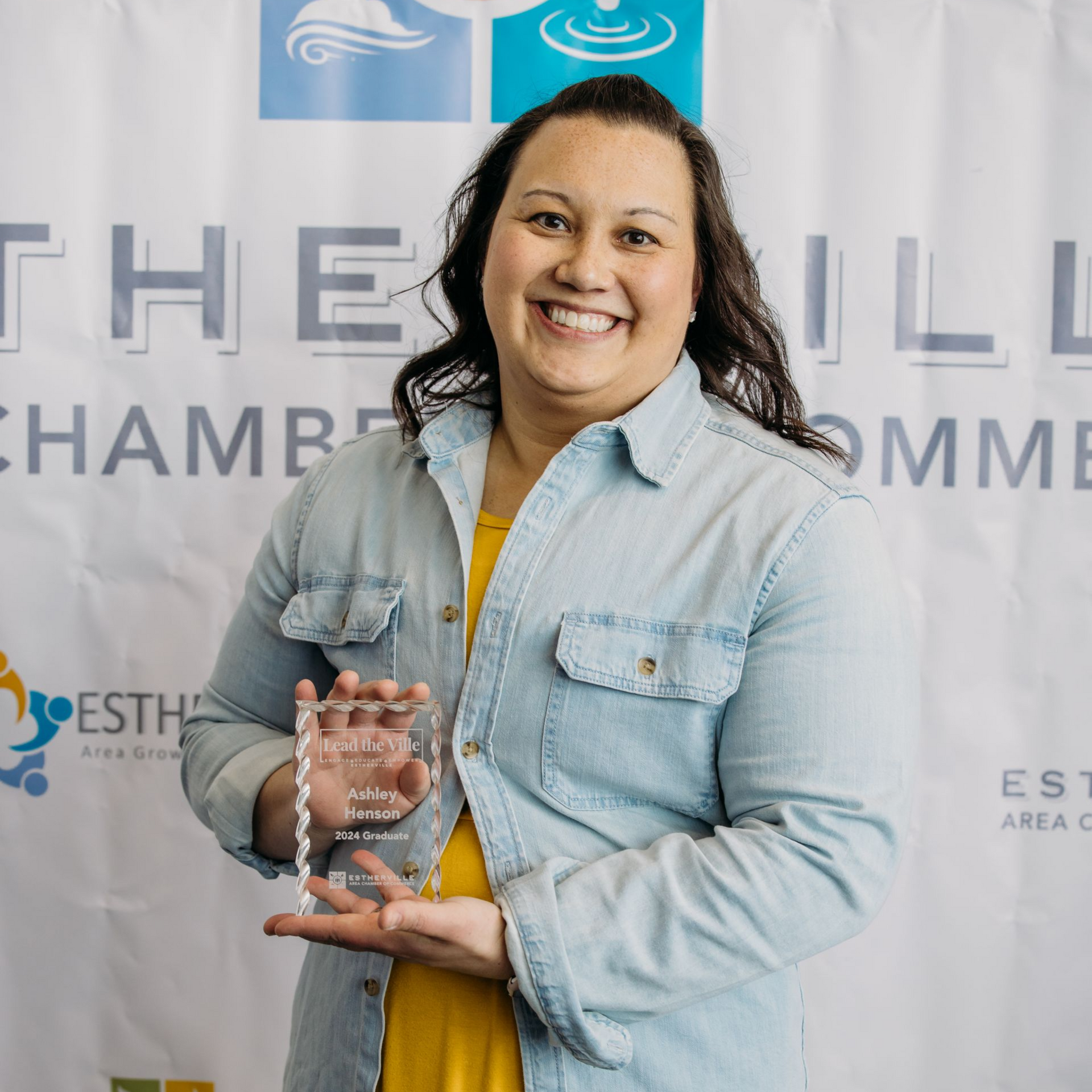 A woman is holding a trophy in front of a colorful backdrop.