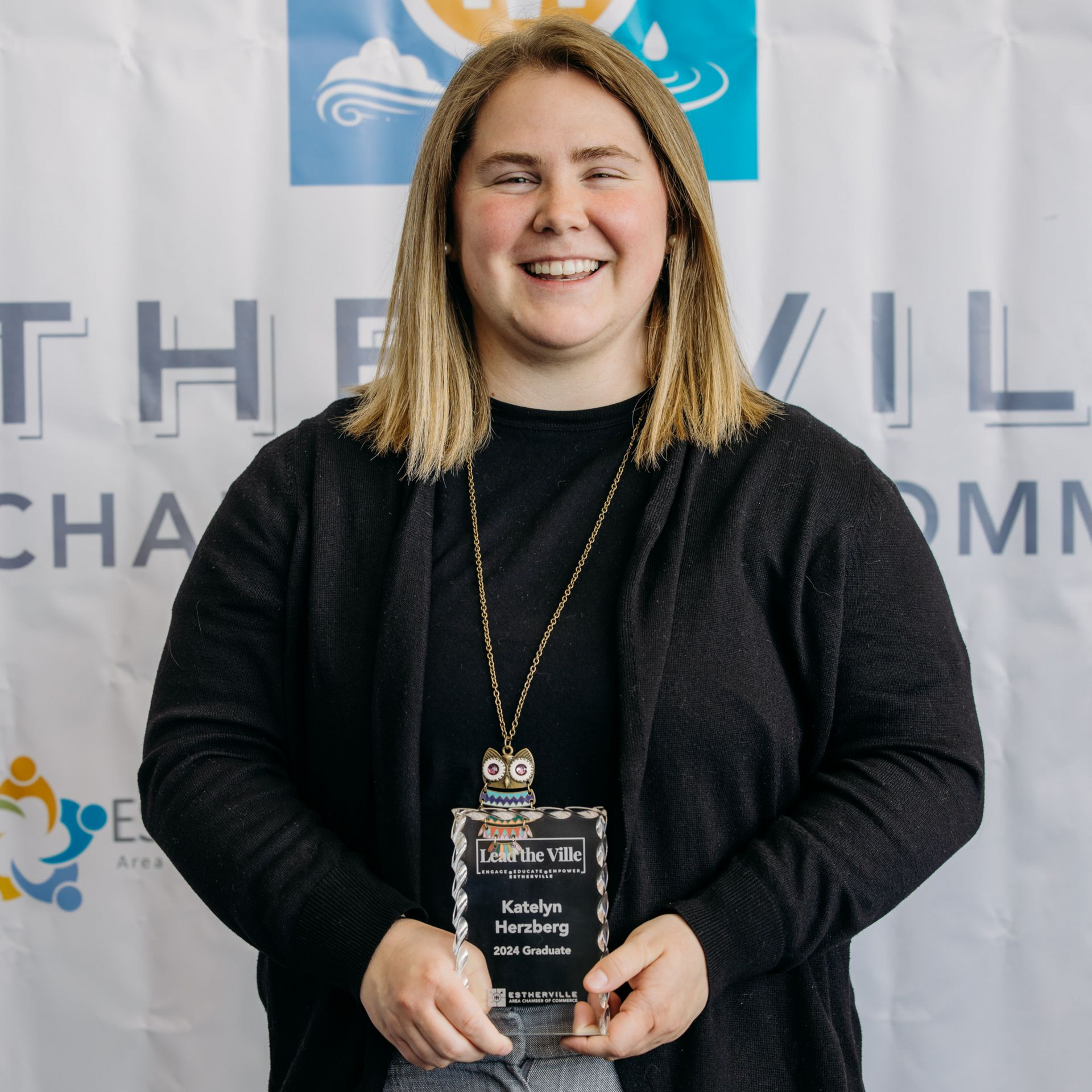A woman is holding an award in front of a wall.