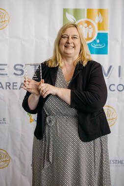 A woman is holding a trophy in front of a white backdrop.