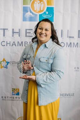 A woman is holding a trophy in front of a colorful backdrop.