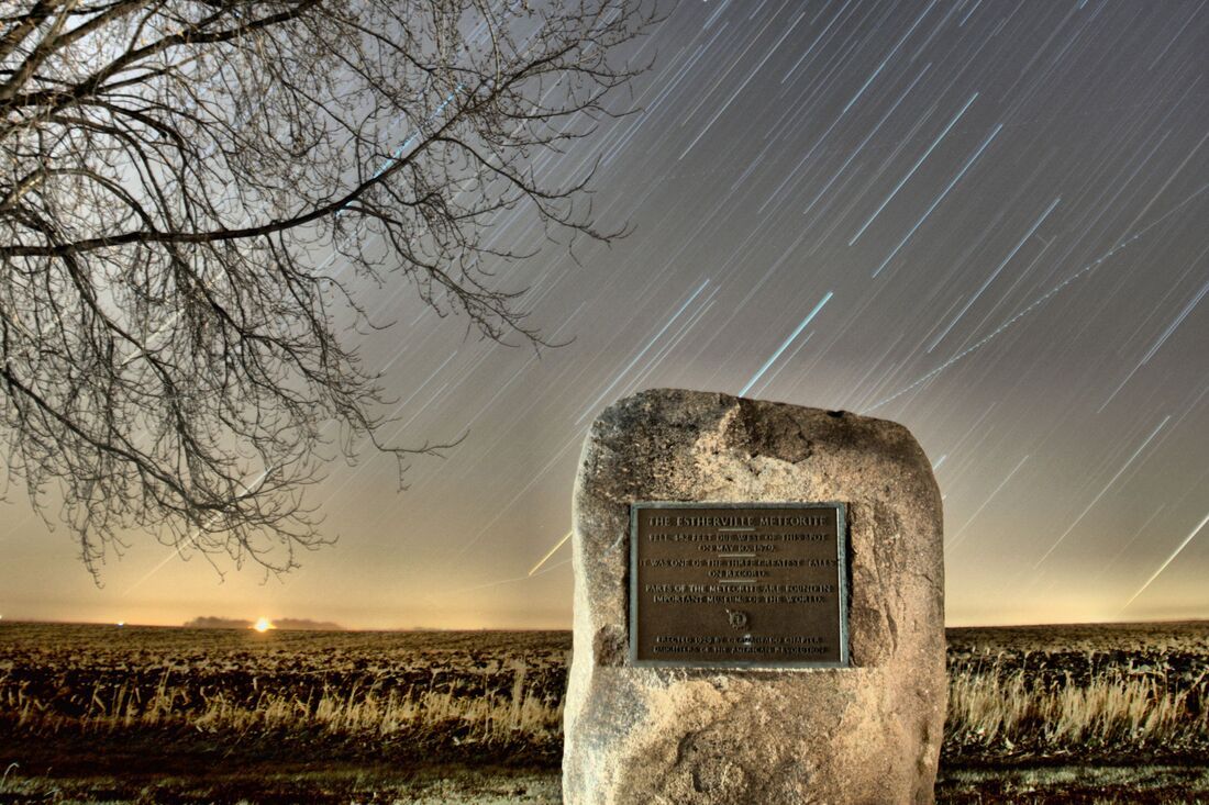 A large rock with a plaque on it is in the middle of a field at night.