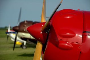 A red propeller plane is parked next to a brown propeller plane.