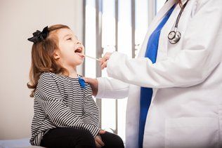 A little girl is having her throat examined by a doctor.