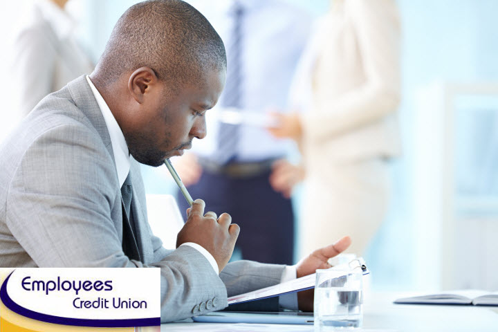 A man in a suit is sitting at a desk writing on a piece of paper.