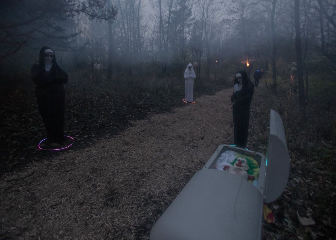 A group of people in ghost costumes are standing next to a coffin in the woods.