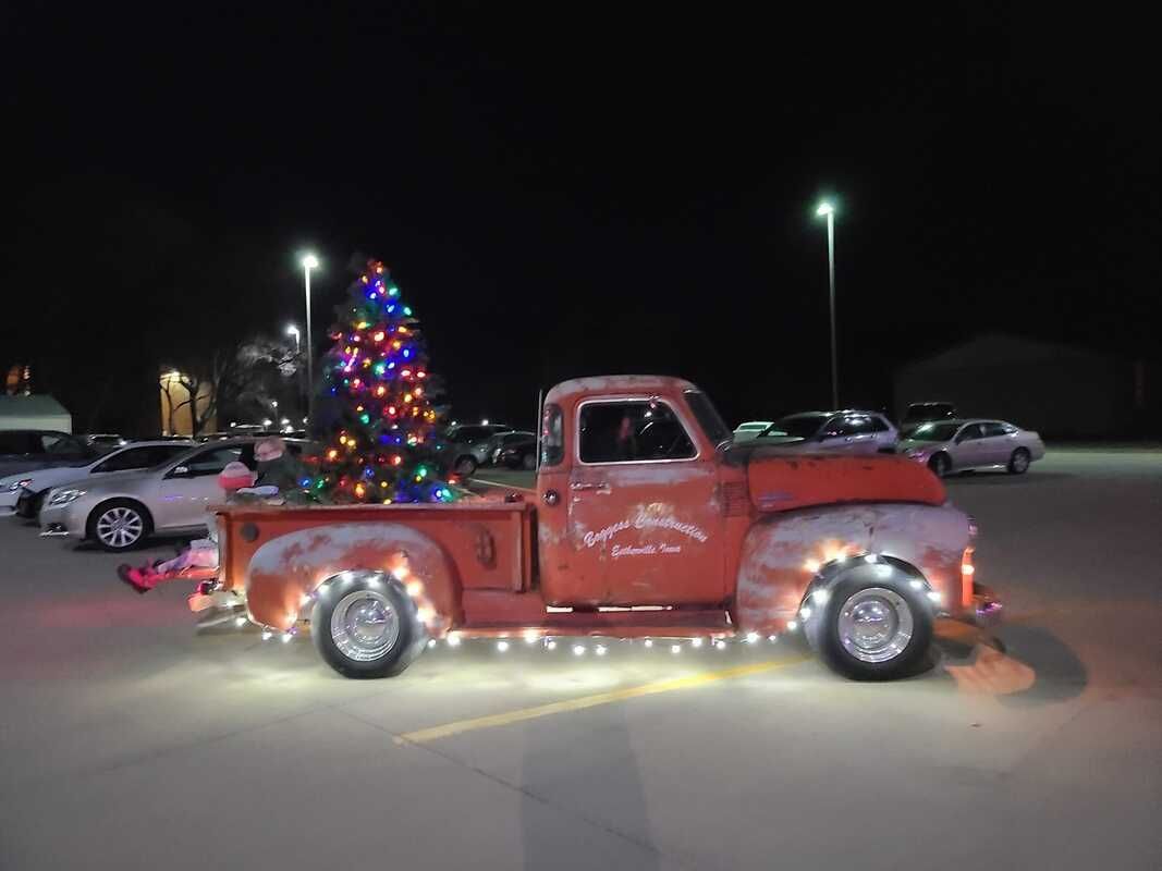 A red truck is decorated with christmas lights and has a christmas tree in the back.