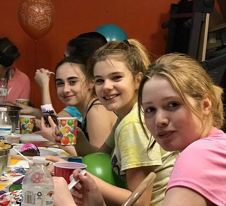 A group of girls are sitting at a table with cups and balloons.