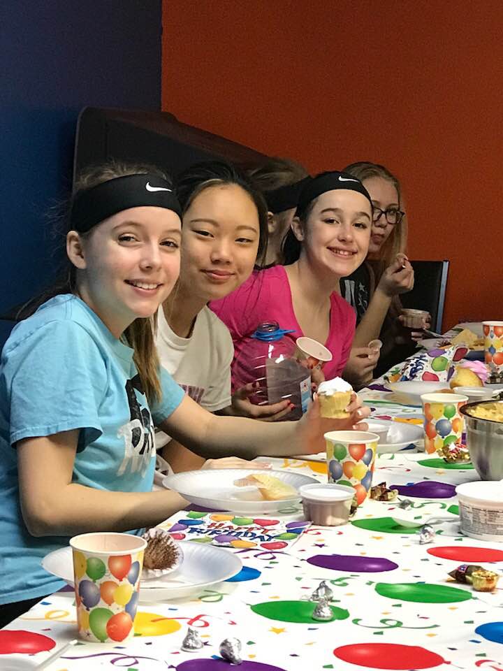 A group of young girls are sitting at a table eating cupcakes.
