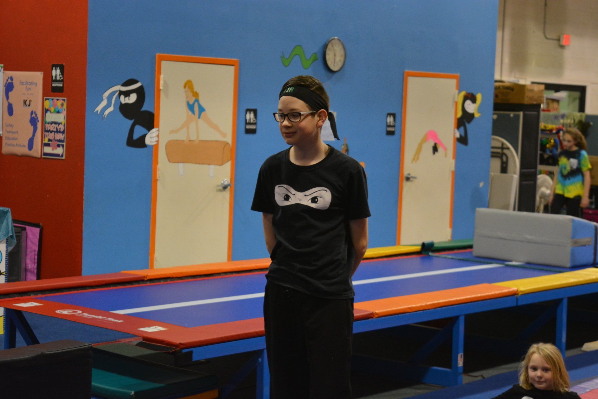 A young boy is standing on a trampoline in a gym.