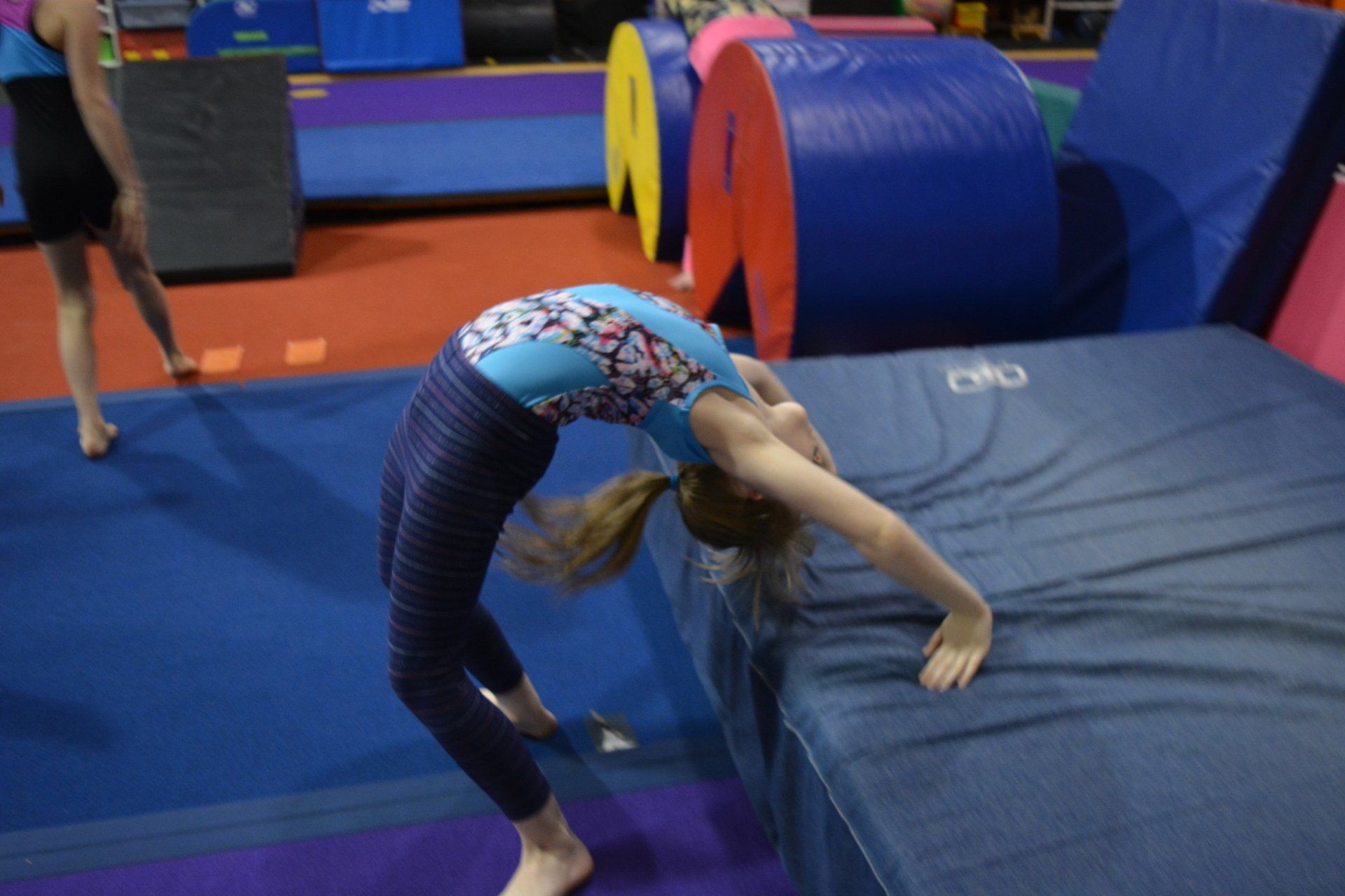 A girl in a blue leotard is doing a handstand on a mat in a gym