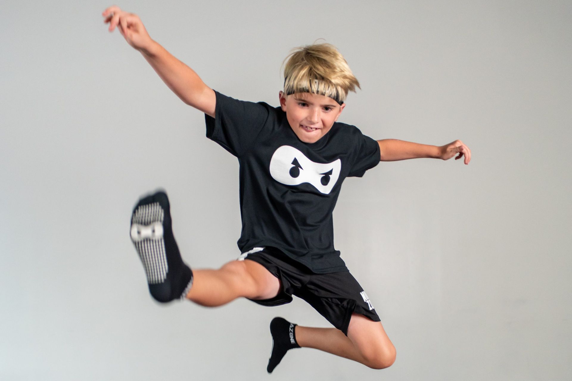 A young boy in a black shirt and black shorts is jumping in the air.