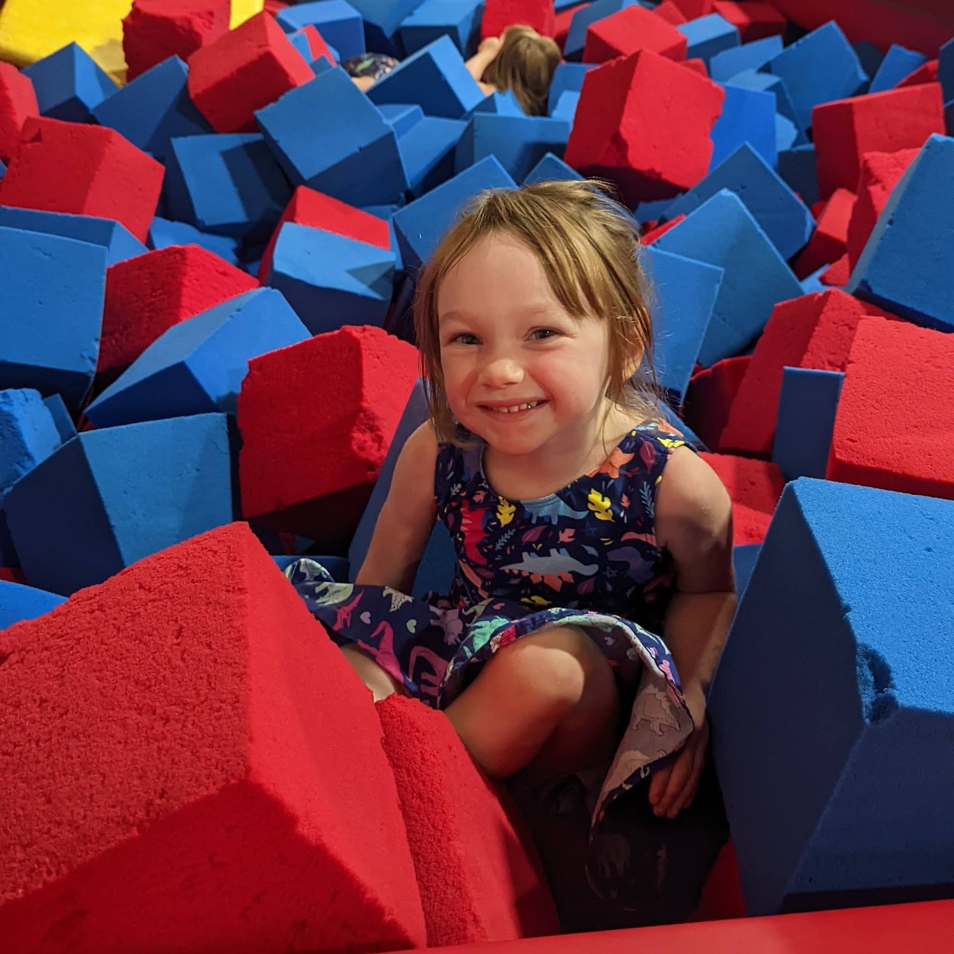 A little girl is sitting in a pile of red and blue foam cubes