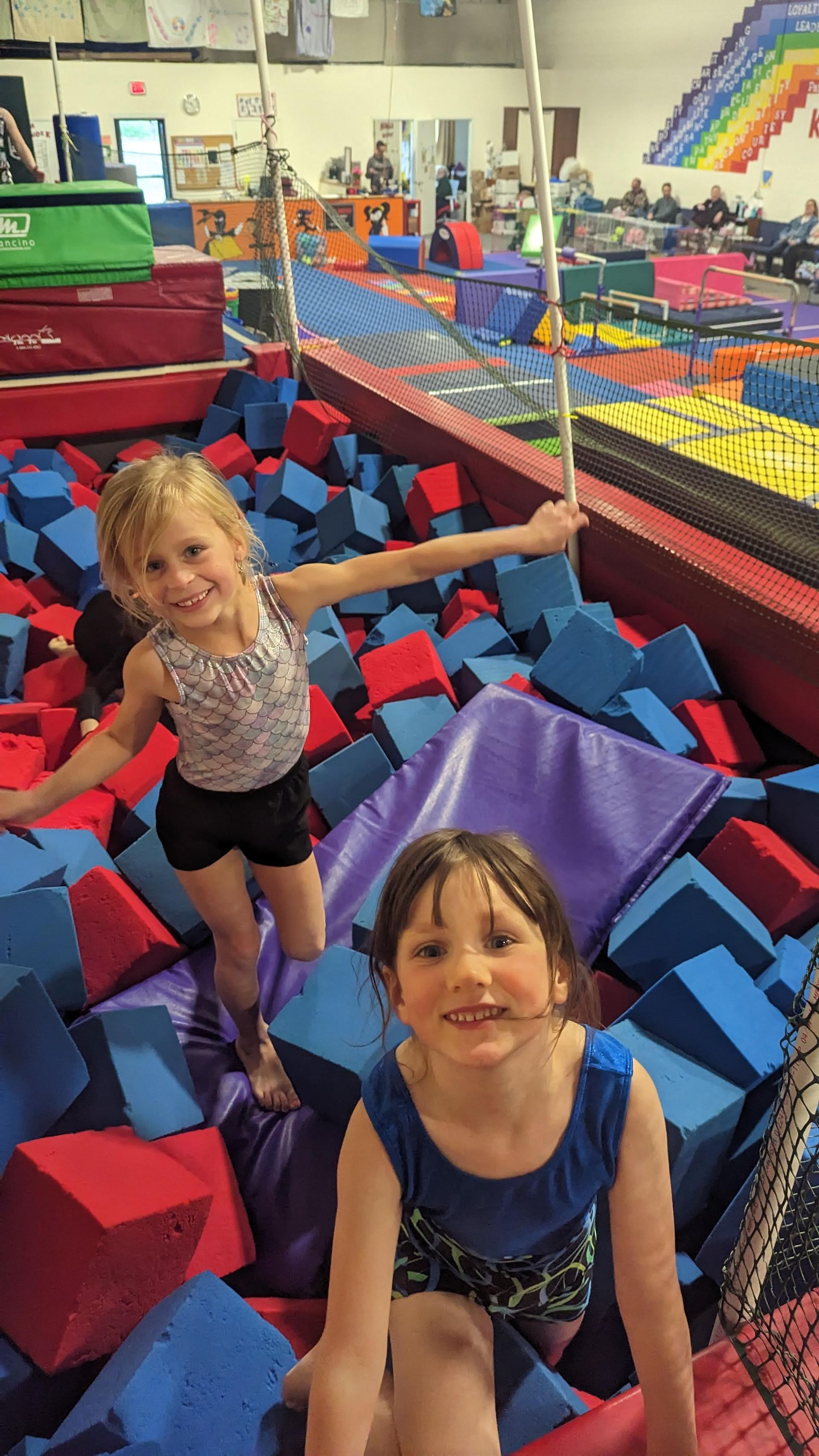 Two young girls are playing in a foam pit at a gymnastics gym.